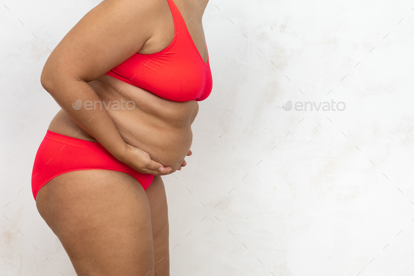 Overweight woman bending down touch hanging belly by hands, free copy  space, white background. Bare Stock Photo by burmistrovaiuliia