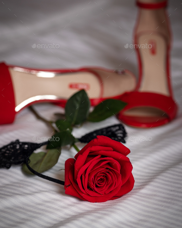 provocative red stiletto heels and red rose lie on the sheet