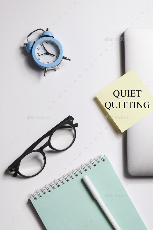quote \'Quiet quitting\' on yellow sticker on computer with clock and notebook.