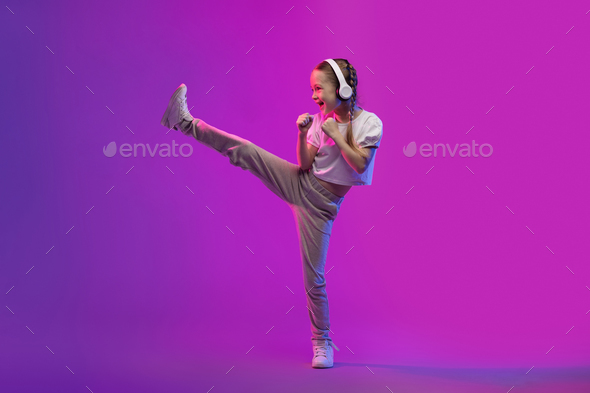 Sweet preteen child girl using wireless headphones and doing karate
