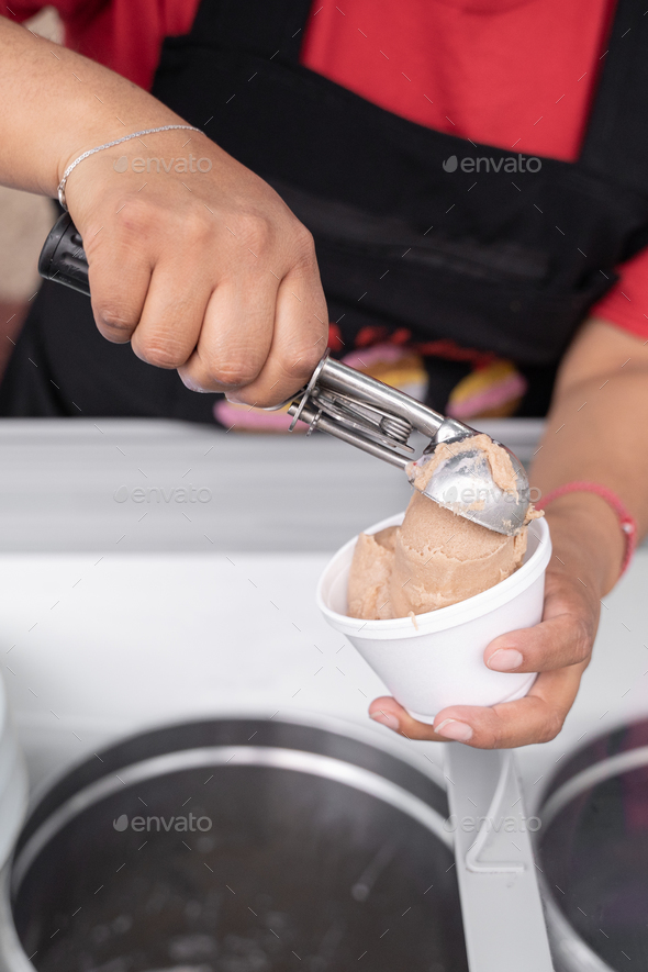 An Hispanic adult woman is serving nut ice cream in a cup in the street