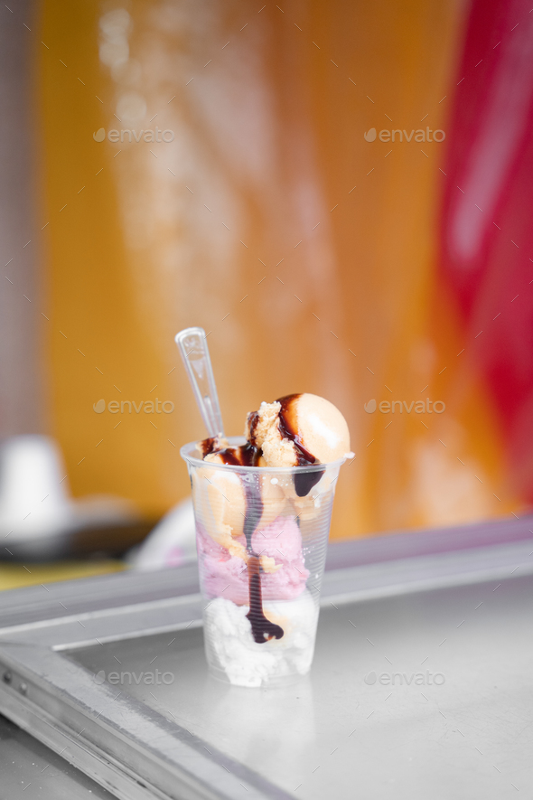 A four ball ice cream served in a plastic cup with a spoon in a street market stall