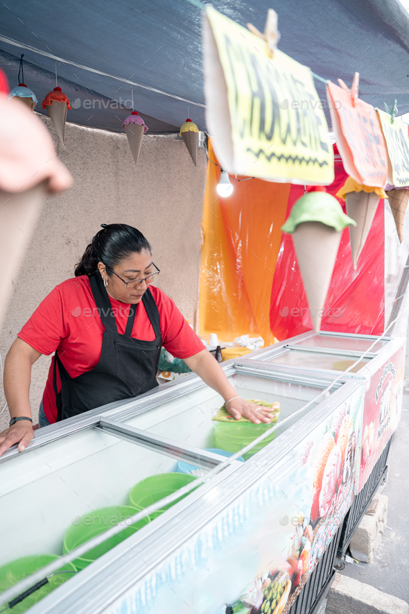 An Hispanic woman is cleaning the ice cream freezer in her street market stall