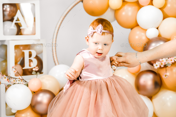 Little redhead baby girl celebrates first birthday anniversary. 1 year family baloons party.