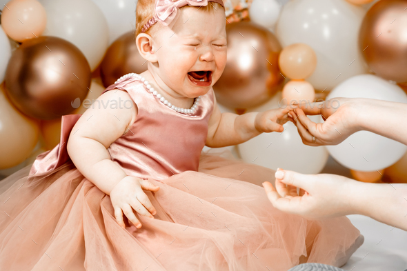 Little crying unhappy redhead baby girl celebrates first birthday anniversary. 1 year family party