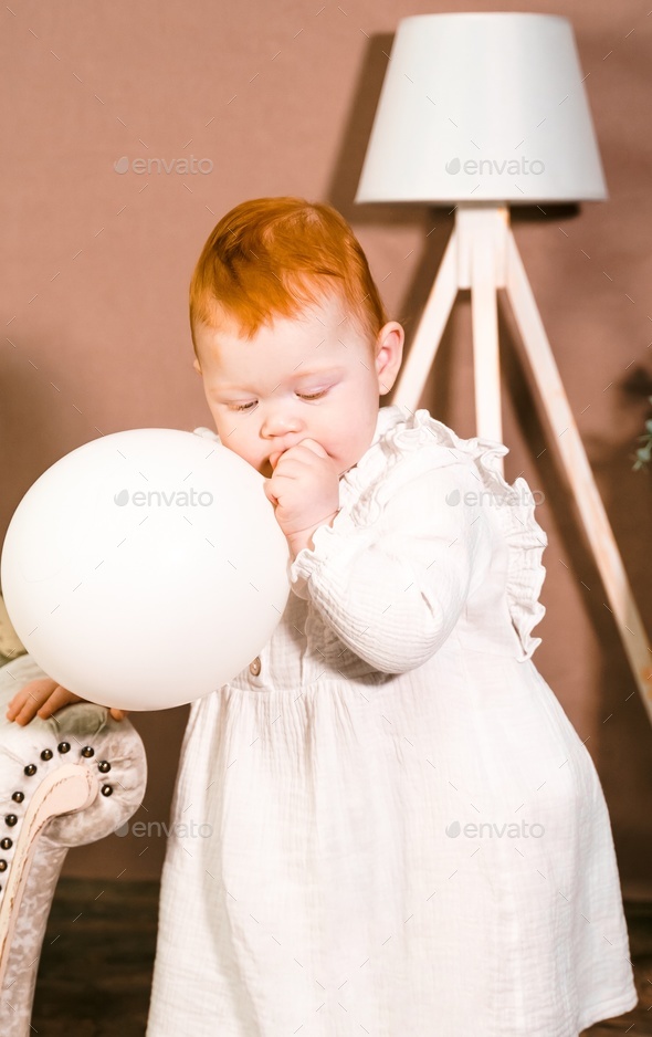 Little redhead baby girl wih balloon celebrates first birthday anniversary. 1 year family party