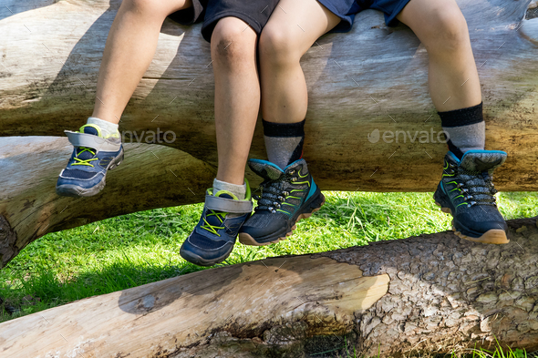 latin kids sitted on a tree trunk with mountain boots.