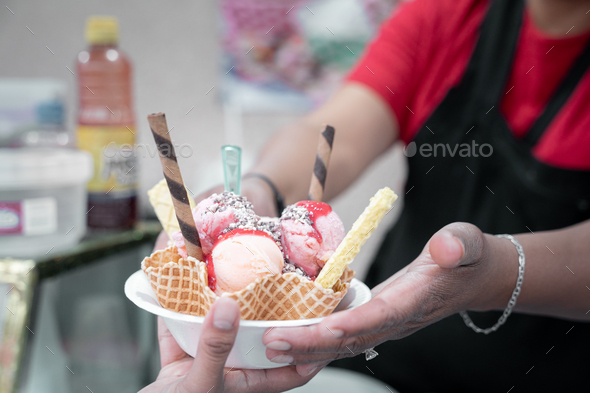 An adult Hispanic woman is serving a traditional Mexican ice cream with toppings to a client