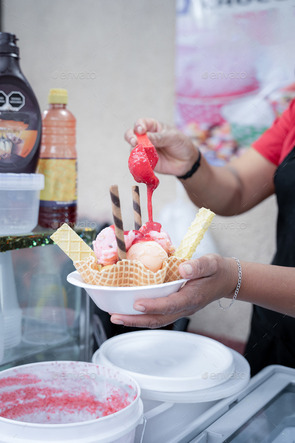 An adult Hispanic woman is pouring mermelade on top of a traditional Mexican ice cream