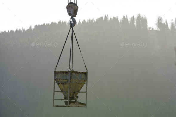 Bucket container with liquid concrete hanging on crane hook