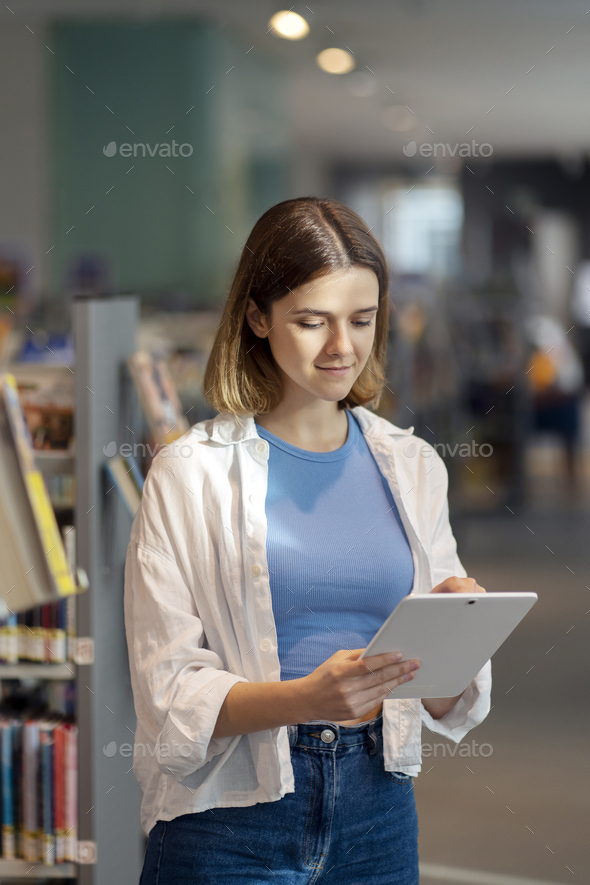 Woman holding digital tablet standing in book store, searching online