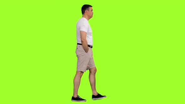 A Man in White T-shirt and Shorts Walks on Green Background alt