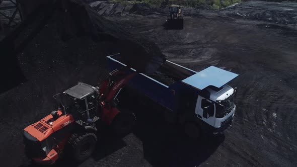 A Powerful Mining Loader Loads a Heavy Dump Truck with Coal Ore