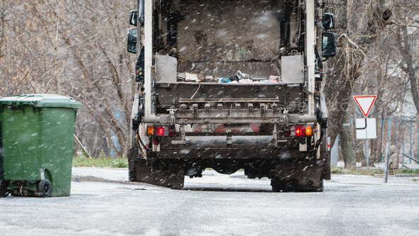 Garbage truck, dustcart with bin lift, household waste removal in residential area in winter