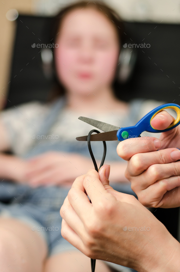 female hands are cutting the headphone cord with scissors, in the background is a girl in headphones