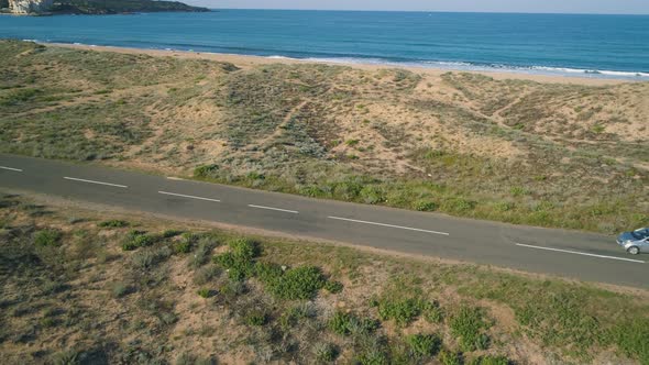 Car Driving Slow at Beach Road Near Turquoise Calm Sea Waters and Golden Sand Dunes in Alepu Beach alt