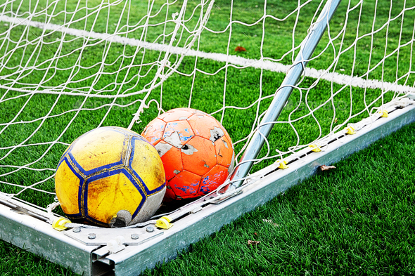 Two ragged shabby soccer balls in the corner of the football goal net