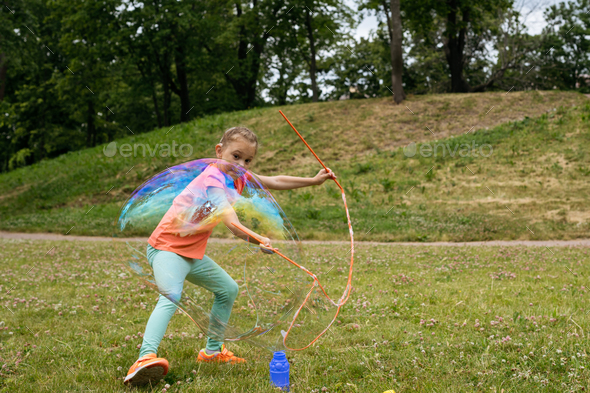 Girl with hearing aid making big soap bubble with special device.