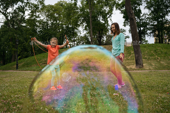 Girl with hearing aid making big soap bubble with special device.