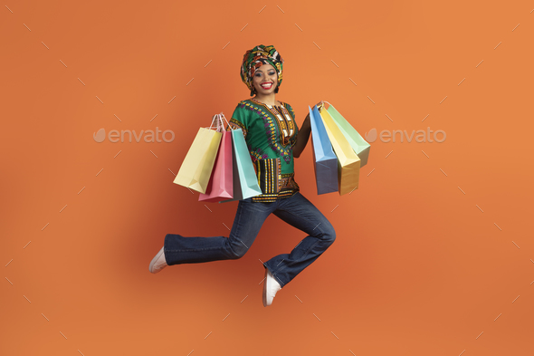 Happy black lady in african costume jumping with her purchases