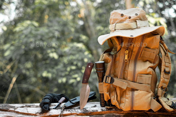 Equipment for survival bucket hat backpack hiking knife camping flashlight resting on wooden timber