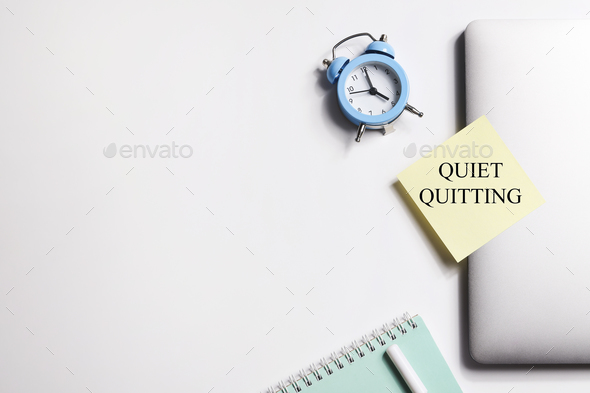 quote 'Quiet quitting' on yellow sticker on computer with clock and notebook. work life balance