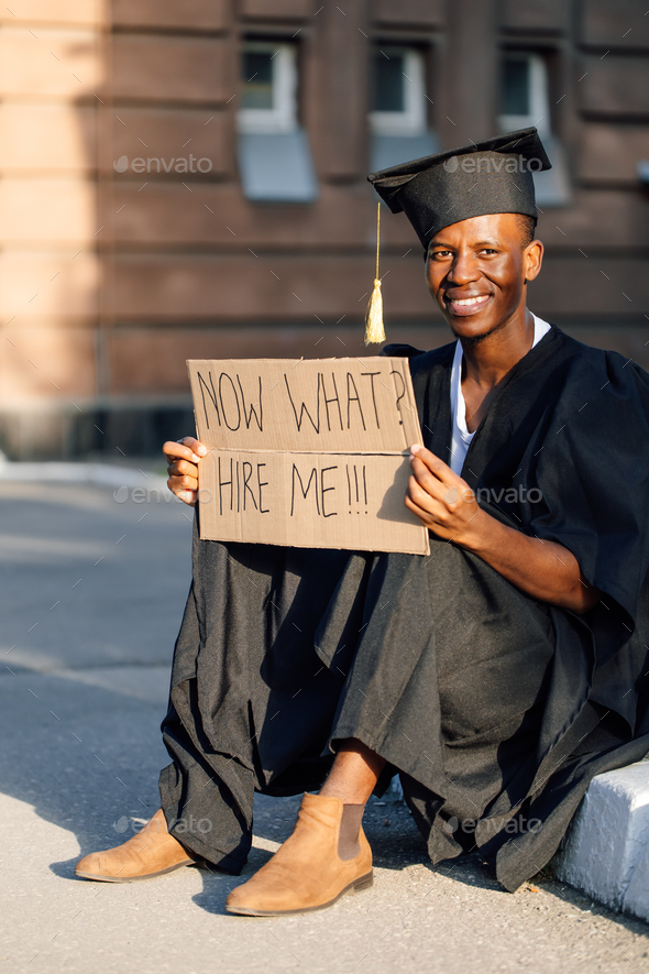 Upset black guy sitting with cardboard poster on street looking for job. University or college