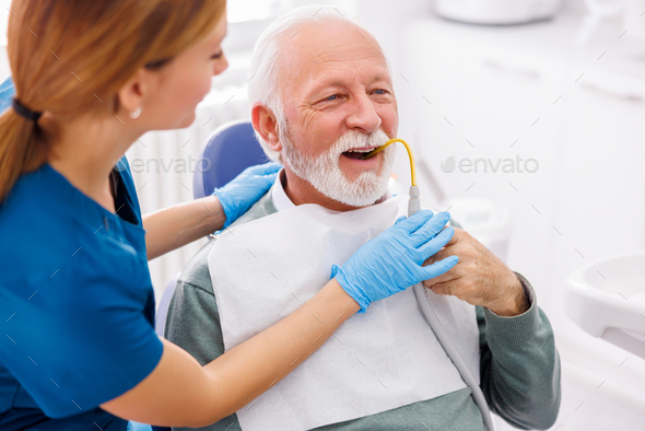Senior man holding saliva suction tube at dentist office