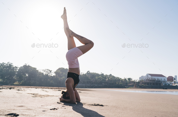 Strong female with athletic body standing on hands and head in asana stretching muscles