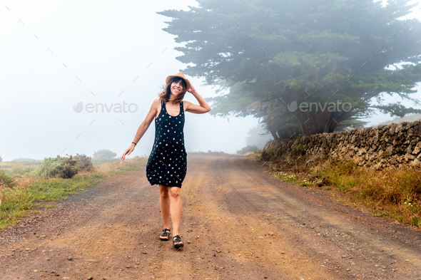 Tourist woman with hat walking through the foggy path towards the juniper forest El Hierro. Canary