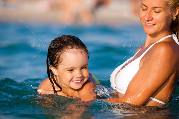 Young mother standing in water and helping to swim her small daughter