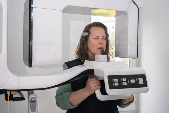 The X-ray technician carefully positions a young woman in front of dental X-ray machine
