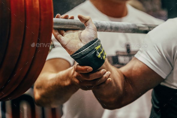 arm powerlifter in wrist wraps to hold heavy barbell before squatting powerlifting competition