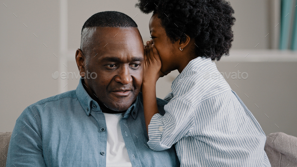 Little African American girl whispers in ear reveals secret to daddy daughter shares secrecy gossip