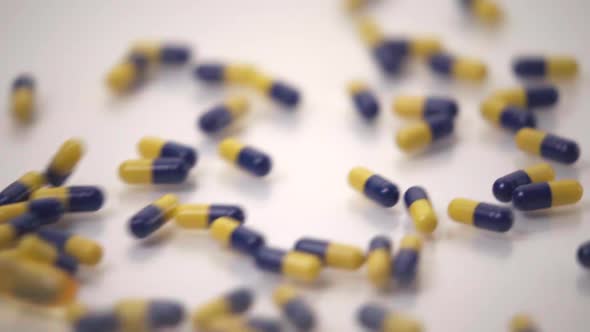 Slow Motion Macro of Blue and Yellow Pills Pushing One Yellow Pill Out of Frame on White Background alt