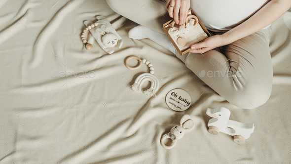 Pregnant woman holding wooden newborn stuff, baby accessories - shoes, toys  on beige background Stock Photo by jchizhe