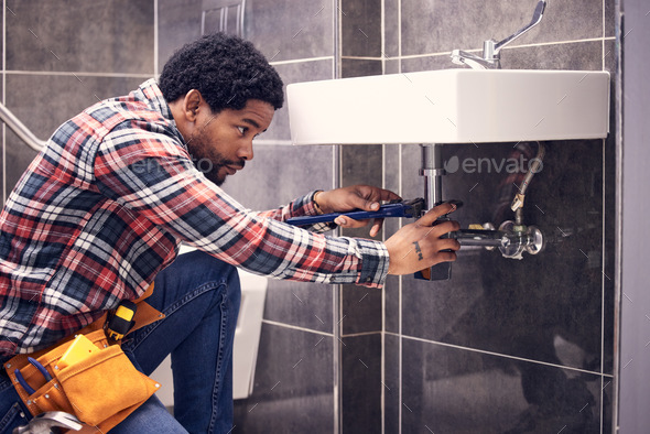 Black man, plumber and maintenance in bathroom, fixing sink pipe with wrench and plumbing industry.