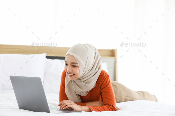 Muslim women lying on bed and using a laptop and waving with friend.