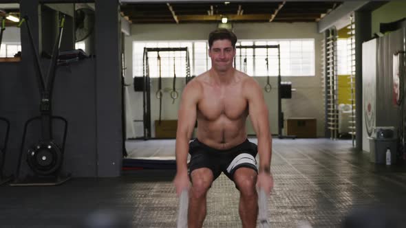 Front view of an athletic Caucasian man working out with battle ropes alt