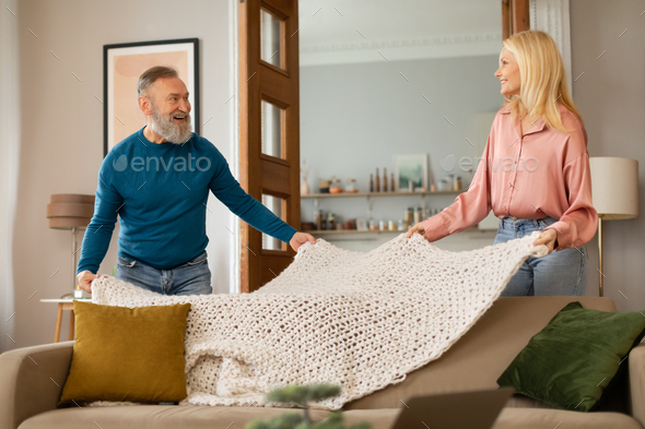 Senior Couple Tidying Room Covering Sofa With Blanket At Home