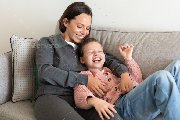 Cheerful european millennial mom hugging little girl, tickling, have fun together, enjoy spare time