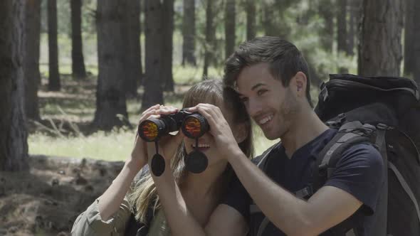 Young couple using binoculars to watch birds in woods