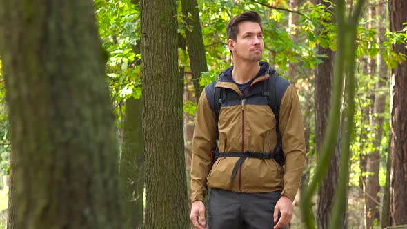 A Young Handsome Backpacker Stands in a Forest and Looks Around alt