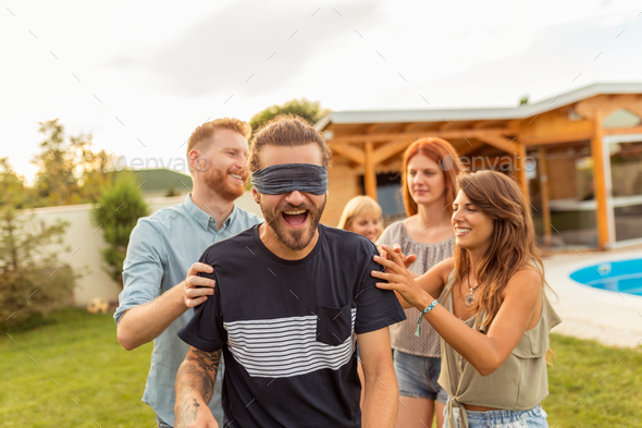 Friends having fun playing blind man\'s buff while at poolside summertime outdoor party