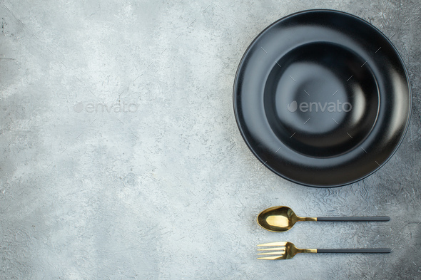 Black dinnerware set and cutlery set on the left side on isolated gray ice background with free