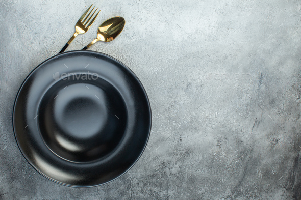 Elegant cutlery set under black dinnerware set on the right side on isolated gray ice background