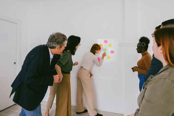 Multi-ethnic business people meeting at office using post it notes to share ideas on white wall
