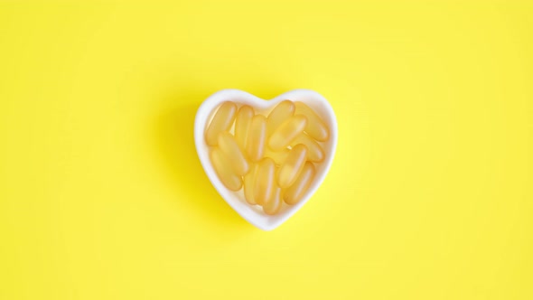 Vitamin D and Omega 3 Fish Oil Capsules Supplement in a Heartshaped Plate on Yellow Background