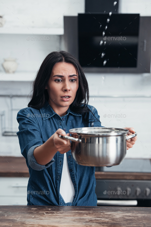 Worried pretty woman with pot dealing with water leak in kitchen