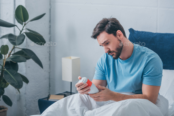 depressed man looking at funeral urn in bed